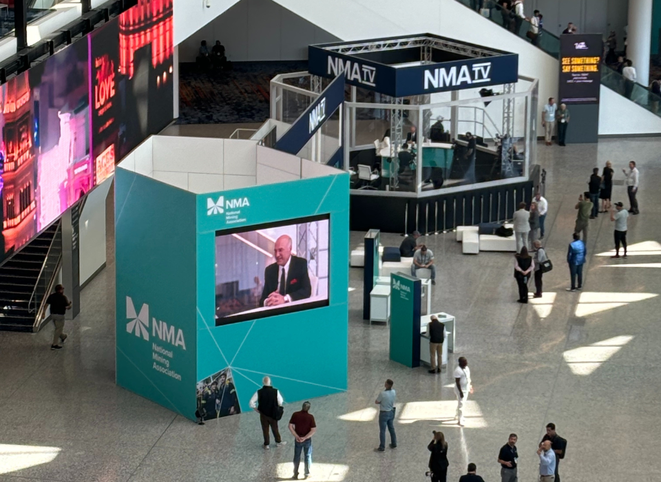 Lobby Of N M A Event With A Group Sitting On A Glossy Black Stage In A High Tech L E D Studio, With Large N M A Branding On Digital Screens Behind Them, Set Up For A Live Broadcast Or Virtual Event.
